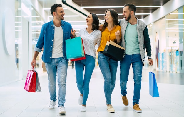 Feliz grupo de amigos elegantes modernos lindos animados no casual wear com sacos de papel está andando no shopping durante as compras.