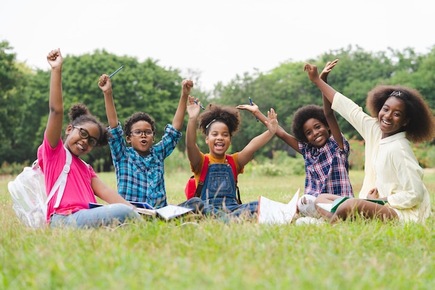 Feliz grupo de crianças afro-americanas levantou as mãos enquanto está sentado no parque