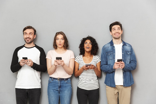 Foto feliz grupo emocional de amigos usando teléfonos móviles mirando a un lado.