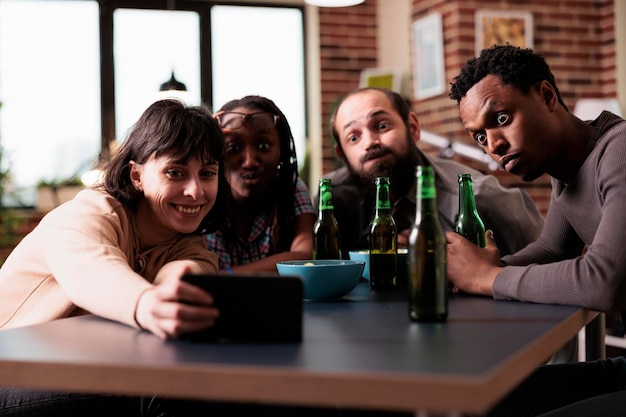 Feliz grupo multicultural de amigos sentados juntos em casa enquanto tira foto selfie com smartphone. Multiétnicas jovens adultos sentados em casa enquanto tiram fotos com o celular.