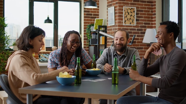 Feliz grupo de personas disfrutando de la estrategia del tablero con cartas y dados, divirtiéndose con el moderno juego competitivo en casa. Hombres y mujeres jugando juegos de fiesta para entretenerse.