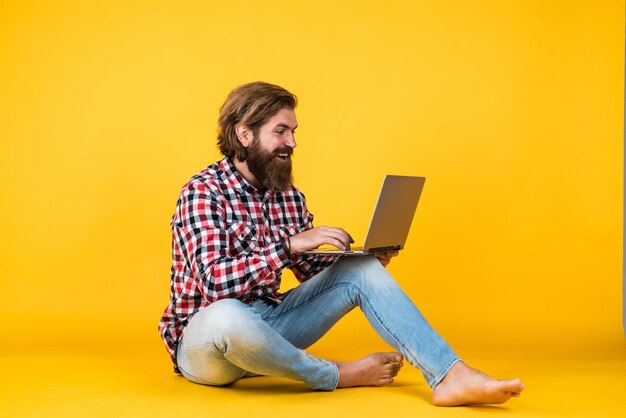 Feliz guapo barbudo con cara sin afeitar y peinado elegante, usa ropa informal trabajando en un cuaderno independiente