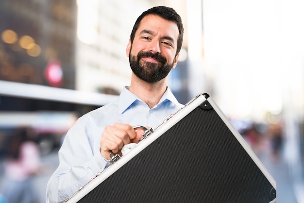 Feliz guapo hombre con barba sosteniendo un maletín sobre fondo desenfocado