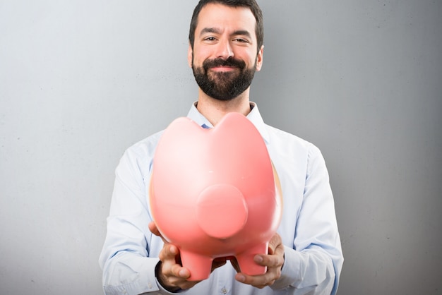 Feliz guapo hombre con barba sosteniendo un piggybank sobre fondo de textura