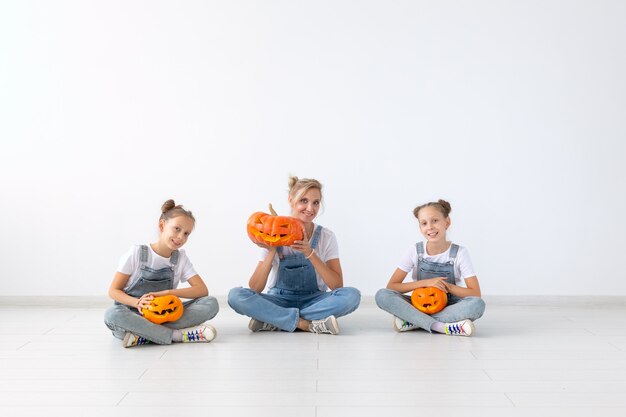 Feliz halloween y concepto de vacaciones: una madre y sus hijas con calabazas. Familia feliz preparándose para Halloween.