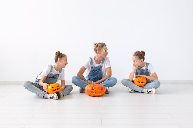 Feliz halloween y concepto de vacaciones: una madre y sus hijas con calabazas. Familia feliz preparándose para Halloween.