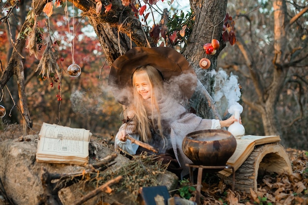 Feliz Halloween. Una linda chica con un disfraz de bruja está en la guarida de la bruja. Linda brujita alegre prepara una poción mágica. Víspera de Todos los Santos.