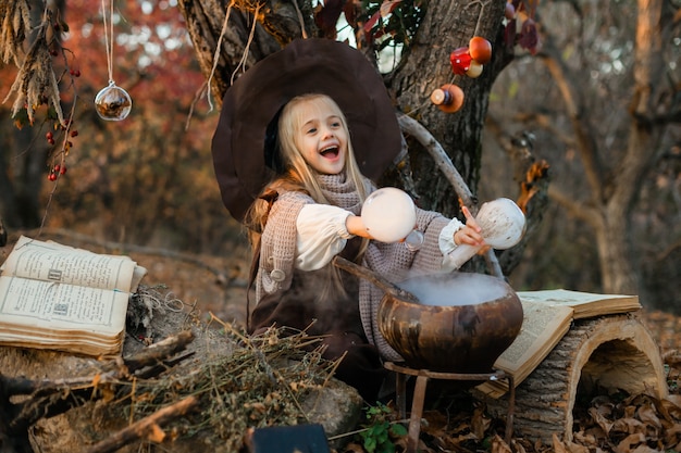 Feliz Halloween. Una linda chica con un disfraz de bruja está en la guarida de la bruja. Linda brujita alegre prepara una poción mágica. Víspera de Todos los Santos.