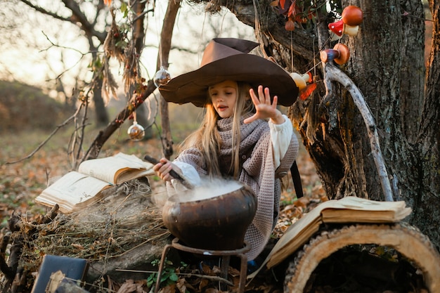 Feliz Halloween. Una linda chica con un disfraz de bruja está en la guarida de la bruja. Linda brujita alegre prepara una poción mágica. Víspera de Todos los Santos.