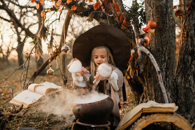 Feliz Halloween. Una linda chica con un disfraz de bruja está en la guarida de la bruja. Linda brujita alegre prepara una poción mágica. Víspera de Todos los Santos.