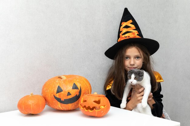 Feliz Halloween Linda niña disfrazada de bruja se sienta con un gato