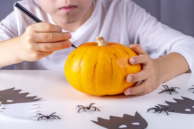 Feliz Halloween. La mano del niño dibuja la cara de calabaza con marcador