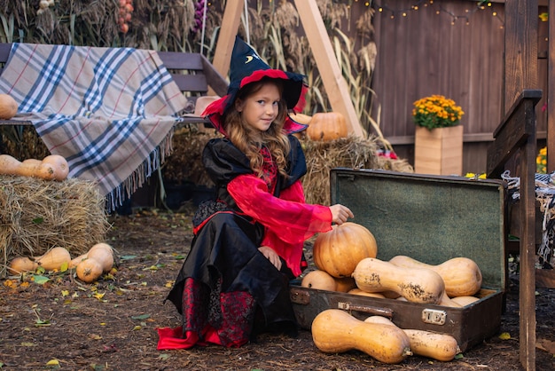 feliz Halloween una niña en un disfraz de bruja con una calabaza divirtiéndose en el otoño cerca de la casa