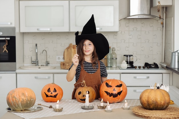 Feliz Halloween Niña linda en traje de bruja con calabaza tallada Familia feliz preparándose para Halloween Niña enciende velas