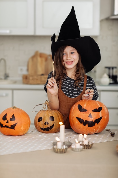 Feliz Halloween Niña linda en traje de bruja con calabaza tallada Familia feliz preparándose para Halloween Niña enciende velas