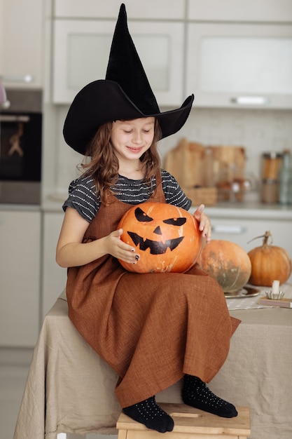 Foto feliz halloween. niña linda en traje de bruja con calabaza tallada. familia feliz preparándose para halloween.