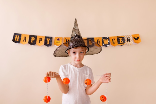 Foto ¡feliz halloween! pequeño mago lindo con una calabaza sobre fondo beige.