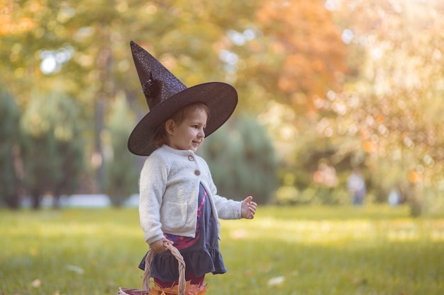 Feliz Halloween. Retrato de niña linda con sombrero de bruja en el bosque de otoño.