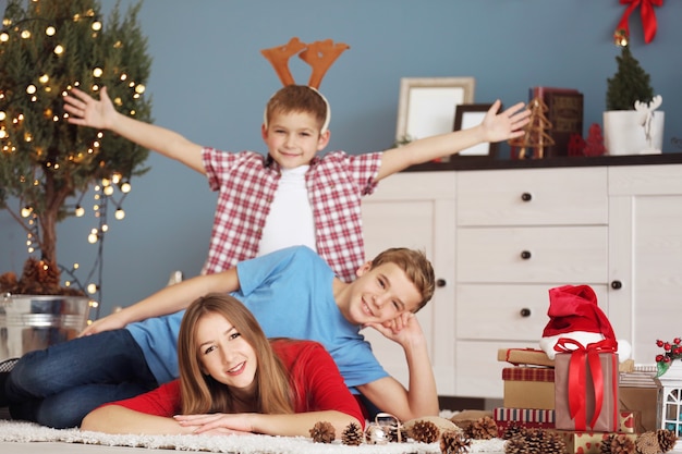 Feliz hermana y hermanos con regalos en el suelo en la sala de Navidad decorada