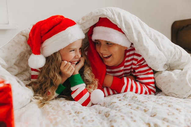 Feliz hermano y hermana con sombreros de Año Nuevo, acostarse debajo de una manta en pijama de Año Nuevo. Navidad y Año Nuevo.