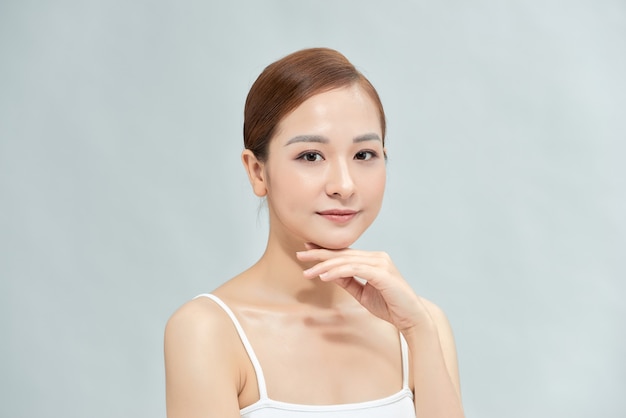 Feliz hermosa chica asiática con la piel fresca en fondo blanco. Expresiones faciales expresivas. Concepto de cosmetología y spa.