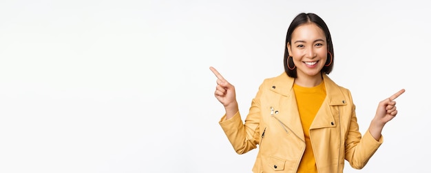 Feliz hermosa chica asiática señalando con el dedo a la izquierda y a la derecha mostrando el logotipo de la pancarta que demuestra la venta de pie en una chaqueta amarilla sobre fondo blanco