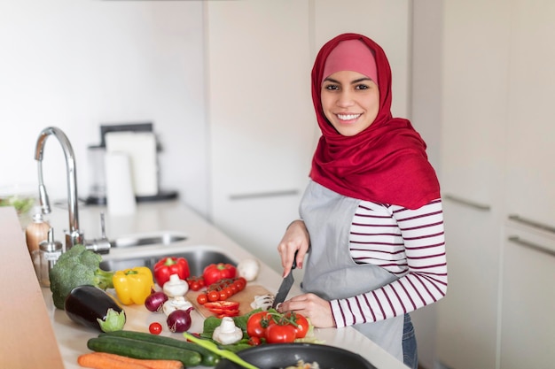 Feliz hermosa esposa musulmana cortando verduras para la cena