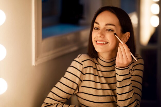 Feliz hermosa joven aplicando maquillaje en casa