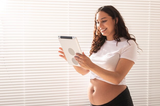 Feliz hermosa joven embarazada hablando con su marido mediante conexión de video y tableta