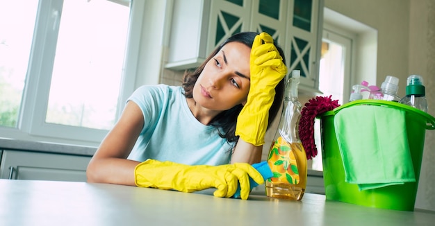 Feliz hermosa joven en guantes amarillos está limpiando la cocina con equipo especial y spray