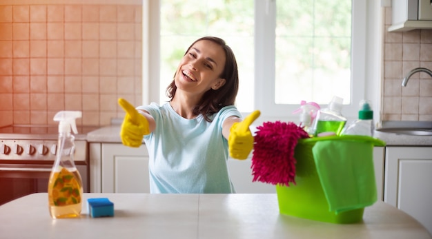 Feliz hermosa joven en guantes amarillos está limpiando la cocina con equipo especial y spray