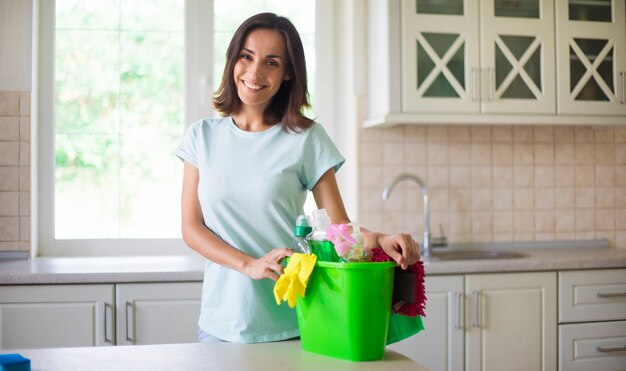 Feliz hermosa joven en guantes amarillos está limpiando la cocina con equipo especial y spray