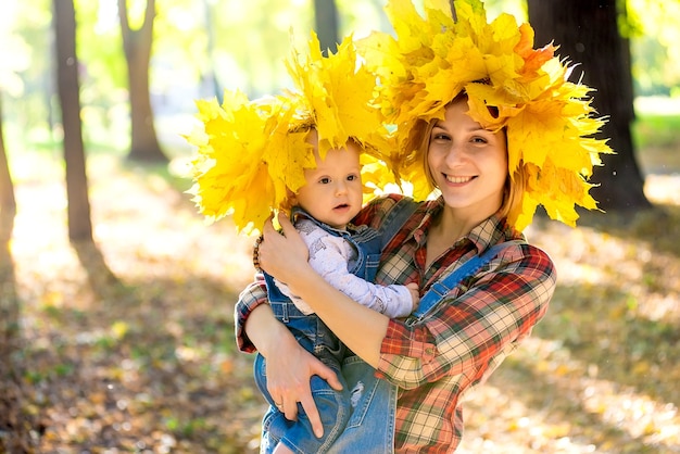 Feliz hermosa joven madre sosteniendo a un niño caminando en el parque en otoño.