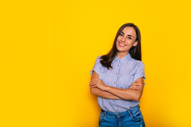 Feliz hermosa joven morena confiada en ropa de sport elegante elegante está posando sobre fondo amarillo