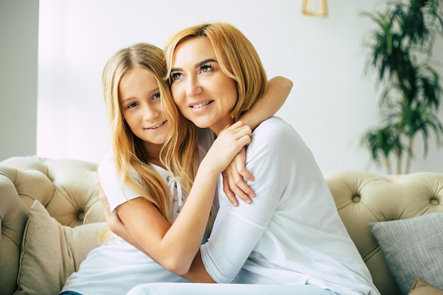 Feliz y hermosa madre e hija pasando tiempo juntas, abrazándose y divirtiéndose mientras se sientan en el sofá de casa. concepto de familia
