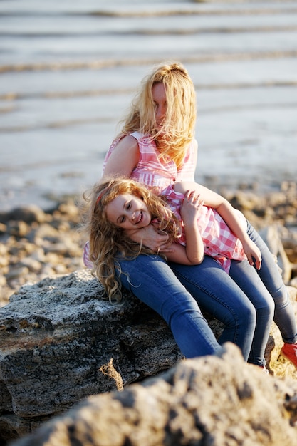 Feliz hermosa madre y su hija divirtiéndose en la playa rocosa al atardecer.