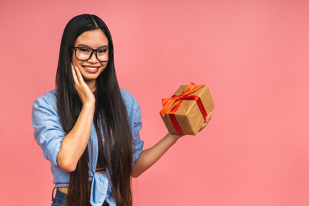 Feliz hermosa mujer asiática sosteniendo caja de regalo aislada sobre fondo rosa Adolescentes enamoradas Recibiendo regalos de los amantes Concepto de Año Nuevo Navidad y Día de San Valentín