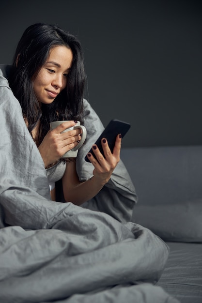 Feliz hermosa mujer asiática sostiene un teléfono inteligente y disfruta del sol de la mañana