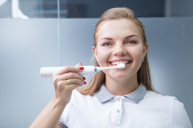 Feliz hermosa mujer dentista sonriendo, sosteniendo el cepillo de dientes eléctrico a los dientes