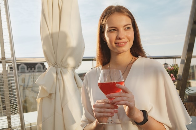 Feliz hermosa mujer disfrutando de beber rosa al atardecer en la terraza del bar