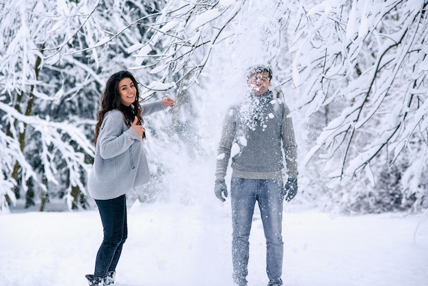 Feliz hermosa mujer embarazada en ropa de abrigo arroja nieve sobre su marido