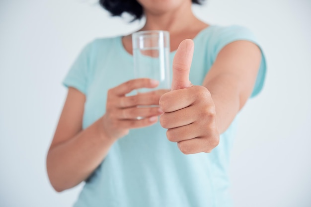 Feliz hermosa mujer joven bebiendo agua Sonriente modelo femenino caucásico sosteniendo vidrio transparente en su mano Primer enfoque en el brazo