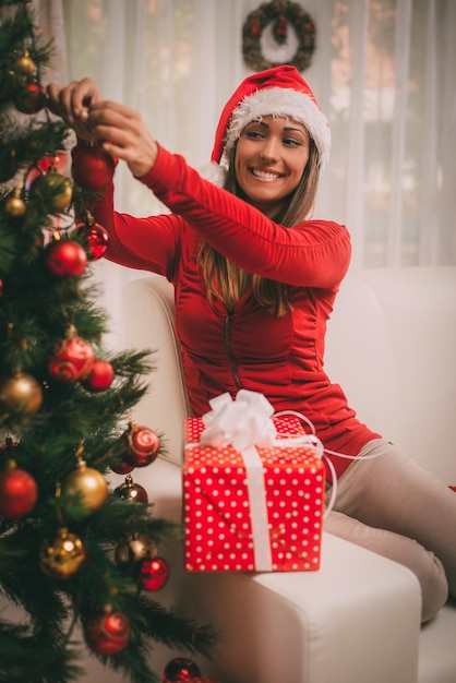Feliz hermosa mujer joven decorando el árbol de Navidad con adornos rojos en casa.