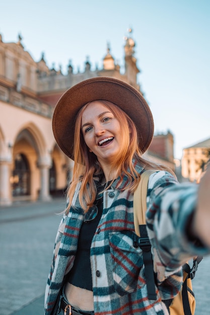 Feliz hermosa mujer joven con hermosa sonrisa con dientes y cabello rubio tomando selfie en la ciudad vieja de Cracovia