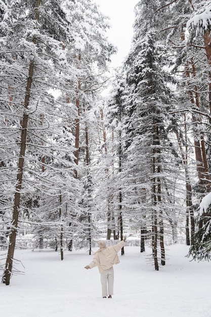 Feliz hermosa mujer joven permanece en suelo nevado en el bosque de invierno Árboles cubiertos por la nieve Fondo de naturaleza pacífica Concepto de felicidad