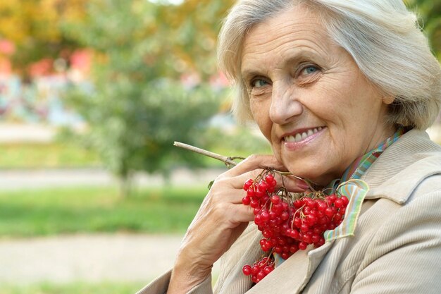 Feliz hermosa mujer mayor en el parque de otoño con viburnum