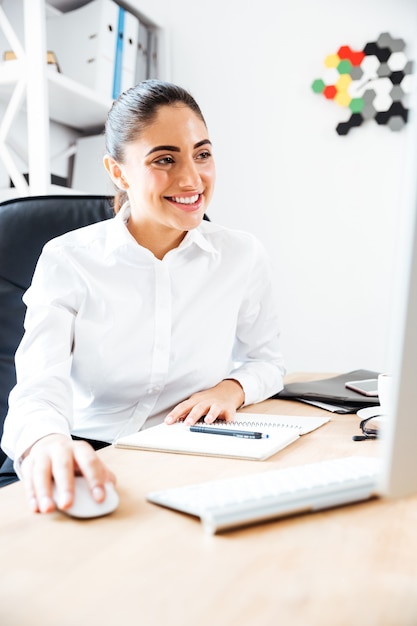 Feliz hermosa mujer de negocios usando la computadora portátil para trabajar mientras está sentado en la oficina