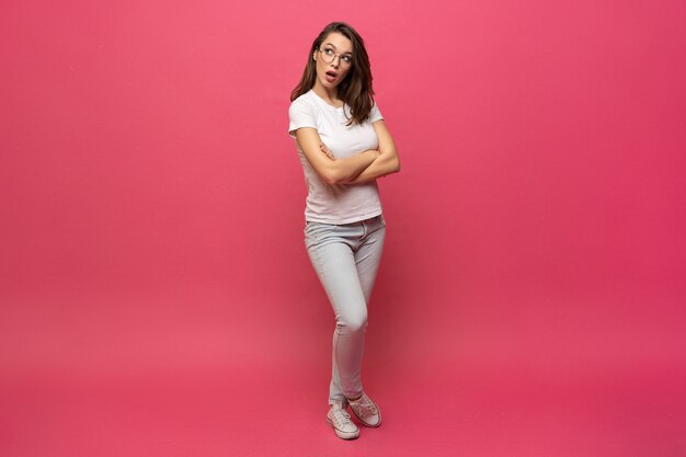 Foto feliz hermosa niña de pie en toda su longitud, aislada sobre fondo rosa.