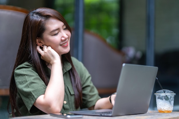 Feliz de hermosas personas independientes asiáticas, mujeres de negocios informales que trabajan con una computadora portátil con una taza de café y un teléfono inteligente en una cafetería como el concepto de comunicación de fondo