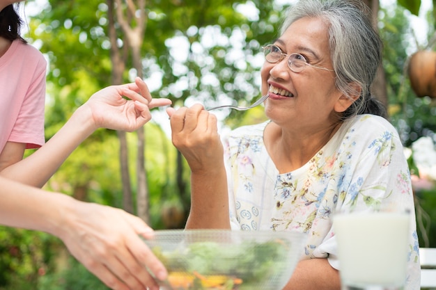 Feliz hija asiática almorzar con su familia y alimentar a la madre con ensalada en el patio trasero.